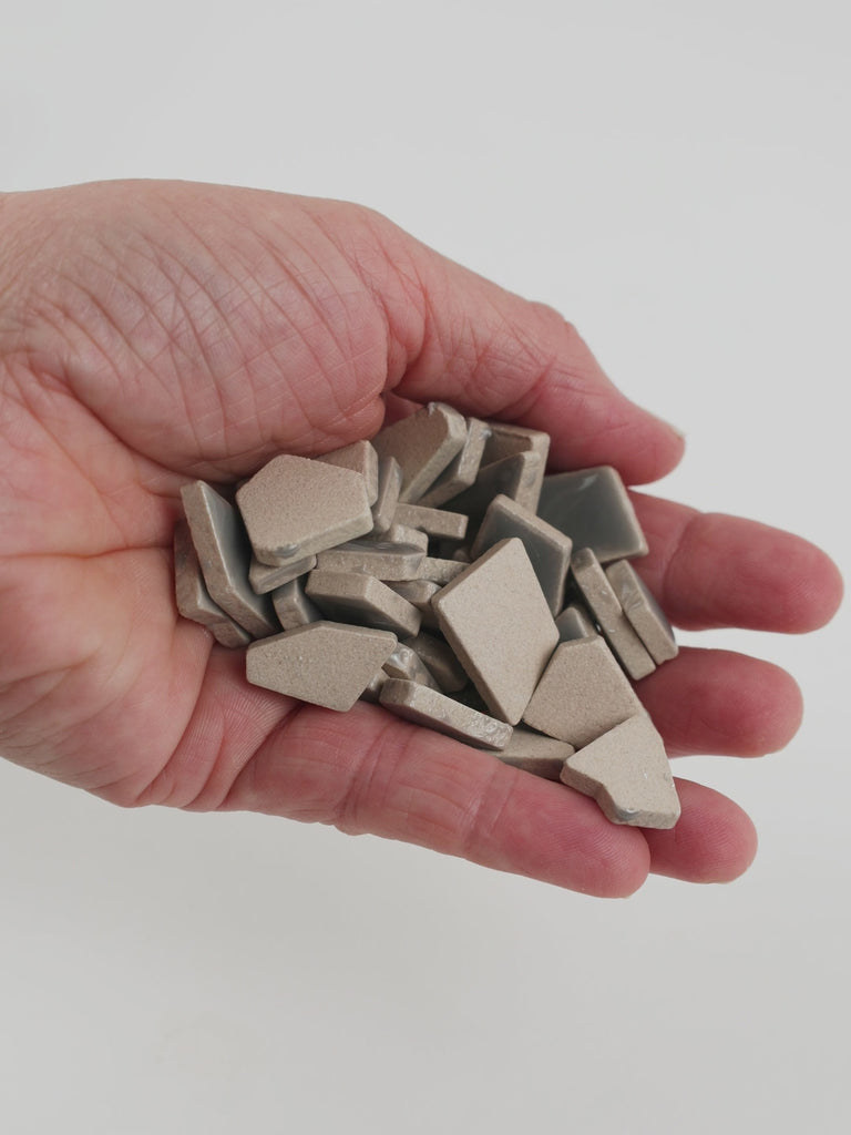 Video of Flip ceramic puzzle pieces in smoke grey, opaque glazed porcelain, 4–20 mm, held in a hand and poured out to show their shapes and finish