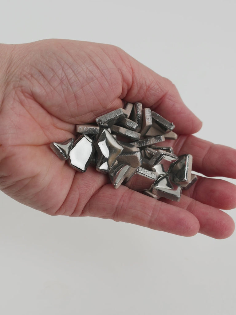 Video of Flip ceramic puzzle pieces in silver, opaque glazed porcelain, 4–20 mm, held in a hand and poured out to show their shapes and finish
