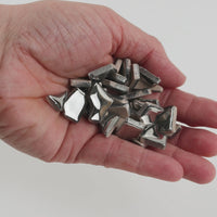 Video of Flip ceramic puzzle pieces in silver, opaque glazed porcelain, 4–20 mm, held in a hand and poured out to show their shapes and finish