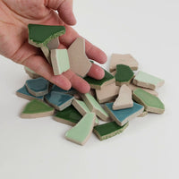 Video of Flip XL ceramic puzzle pieces in green mix, opaque glazed porcelain, 20–60 mm, picked up from a pile by hand and dropped back to show their size, shapes and finish